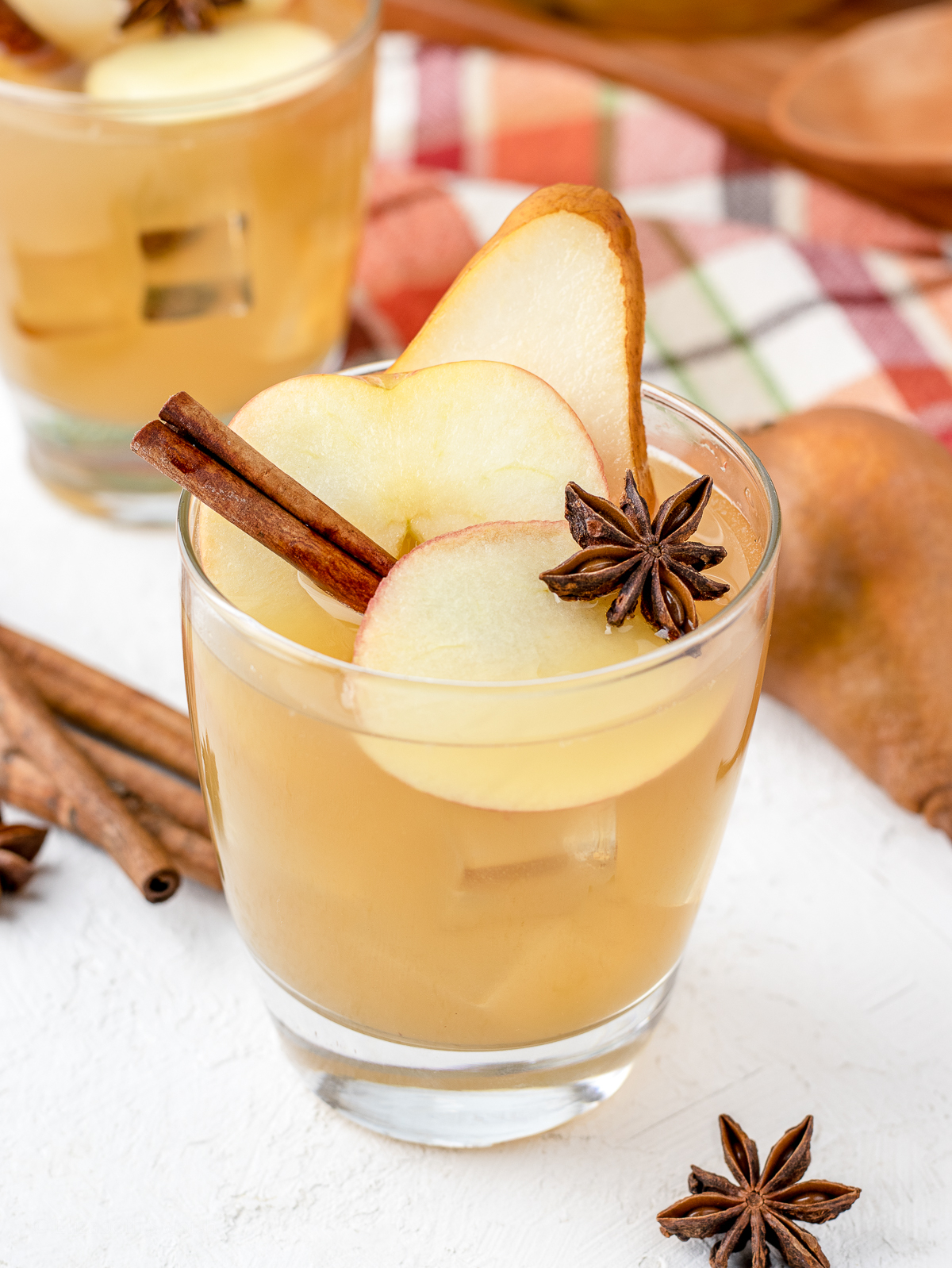 Close up of sangria in a glass garnished with apple slices, pear slice, cinnamon stick, and star anise.