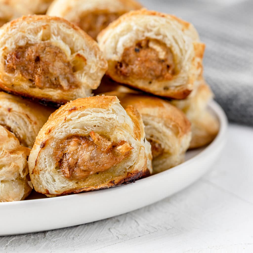 Chicken Sausage Rolls stacked on a white plate.