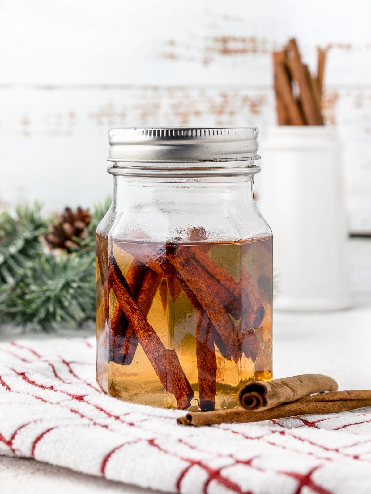 Cinnamon Syrup stored in a glass lidded jar, surrounded by extra cinnamon sticks.