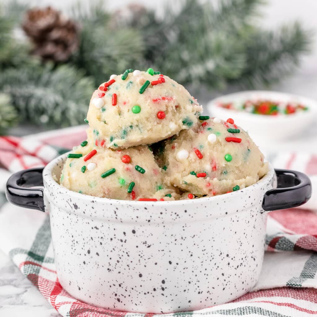 Edible Sugar Cookie Dough in a handled bowl with more sprinkles and a spoon on the side.