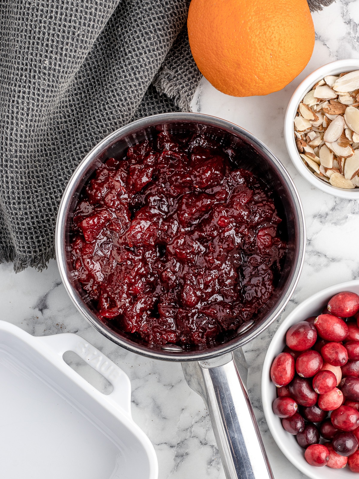 Cranberry Pie Filling in a saucepan surrounded by cranberries, an orange, and slivered almonds.
