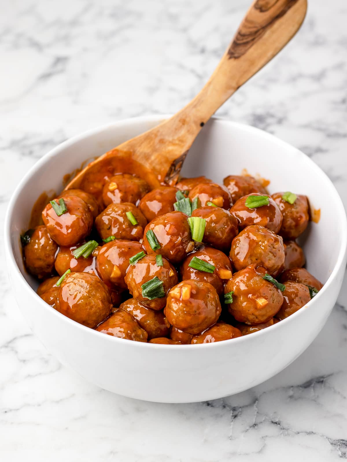 Honey Sriracha Meatballs in a bowl with a spoon for serving.