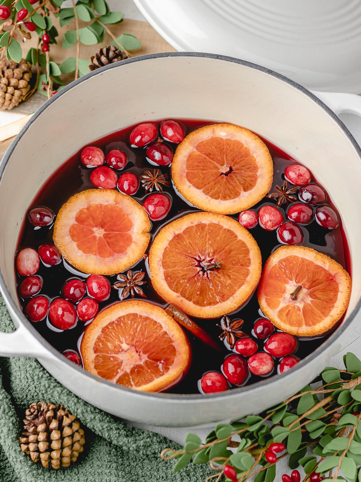 Non Alcoholic Mulled Wine in a Dutch oven with orange slices, cranberries, cinnamon sticks, star anise, and cloves floating.
