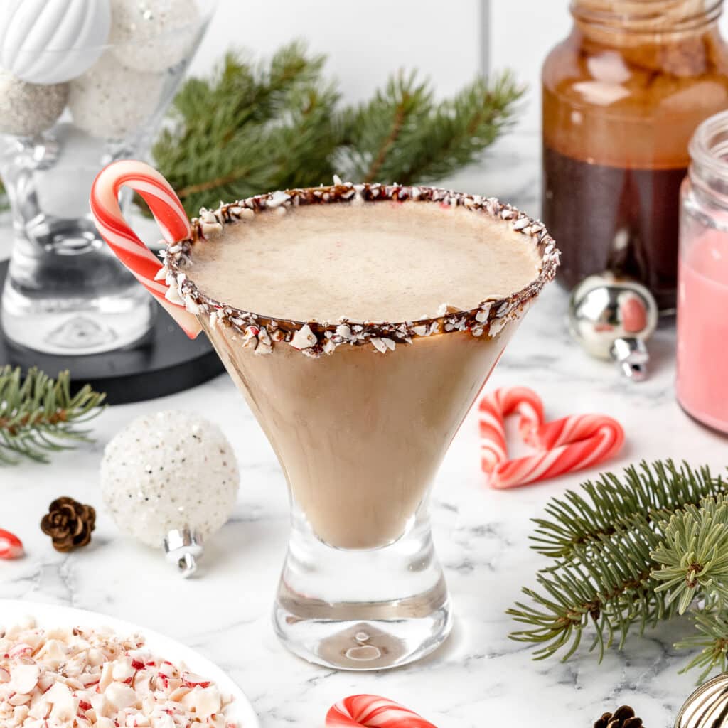 Peppermint White Russian Mocktail in a martini glass with a chocolate syrup and crushed candy cane rim. Mini candy cane on the side.