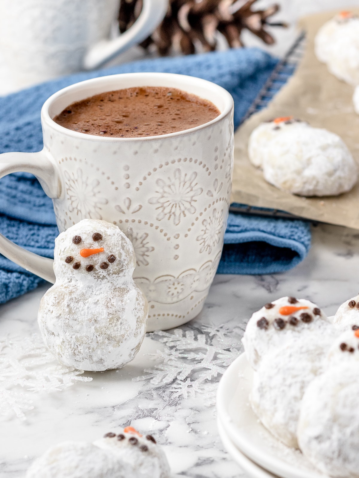 Snowman Snowball Cookie leaning against a cup of hot cocoa.