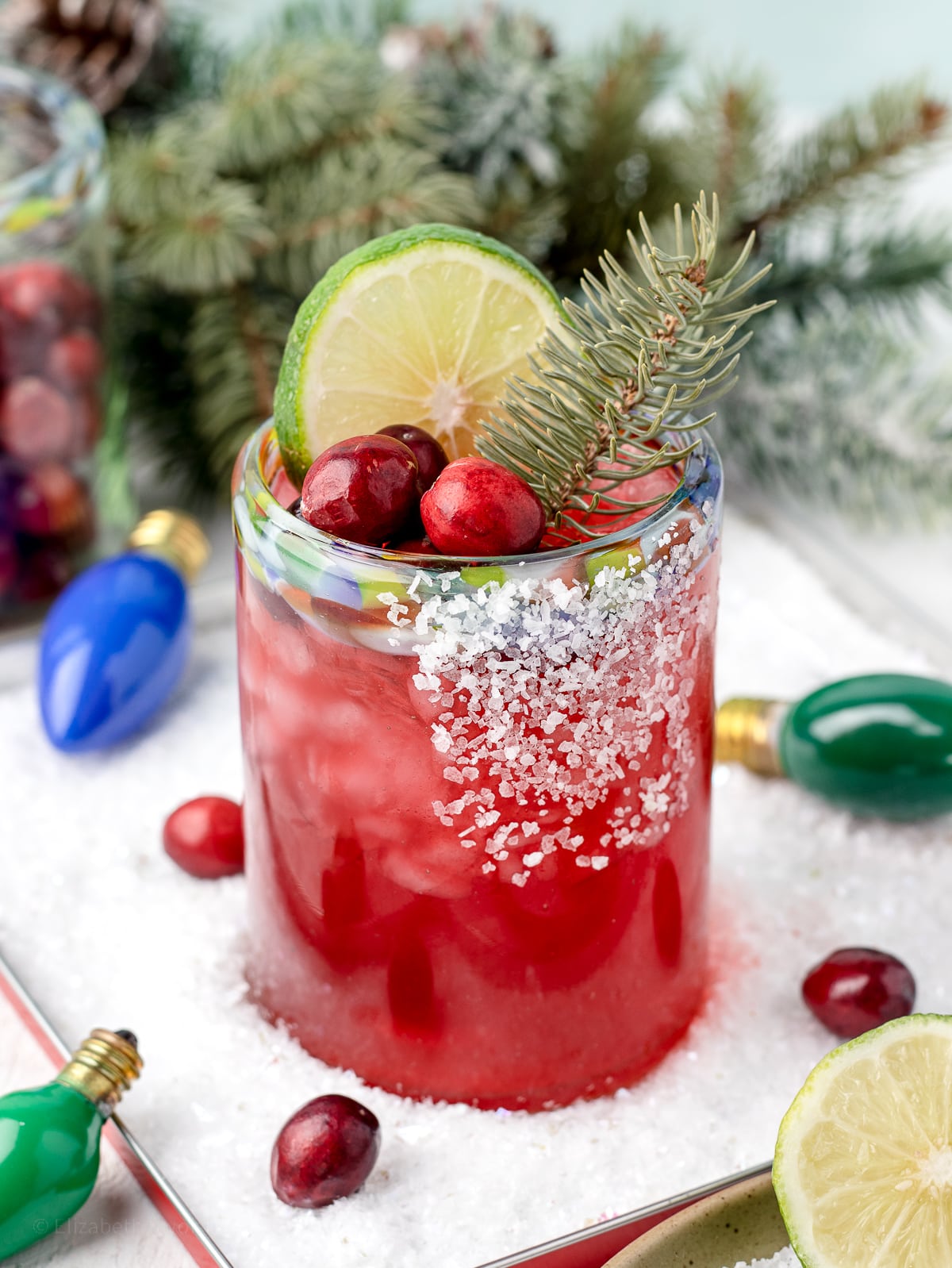Cranberry Margarita Mocktail sitting in a dish of snow and surrounded by Christmas lights and pine branches