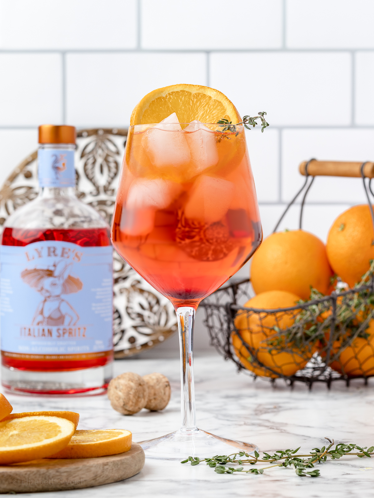 Non alcoholic Aperol spritz garnished with an orange slice and a sprig of fresh thyme.