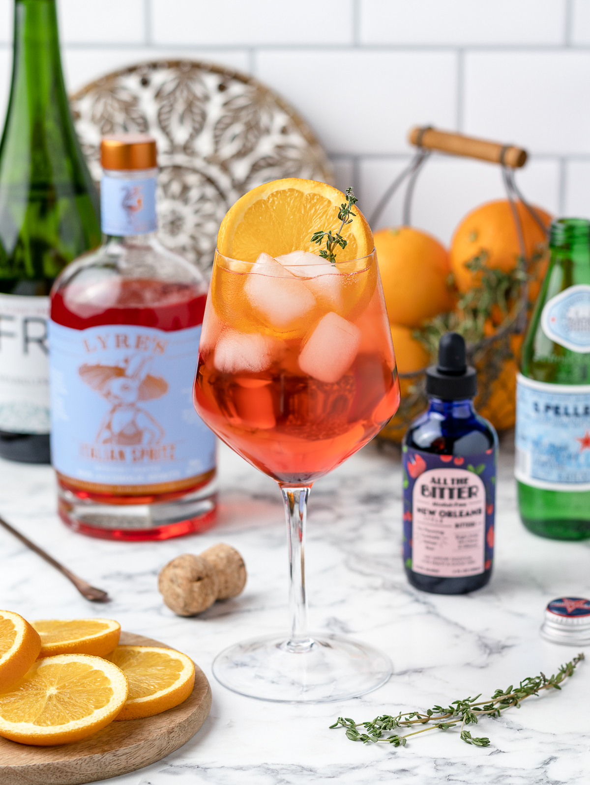 NA Aperol Spritz surrounded by orange slices, thyme, and other ingredients.