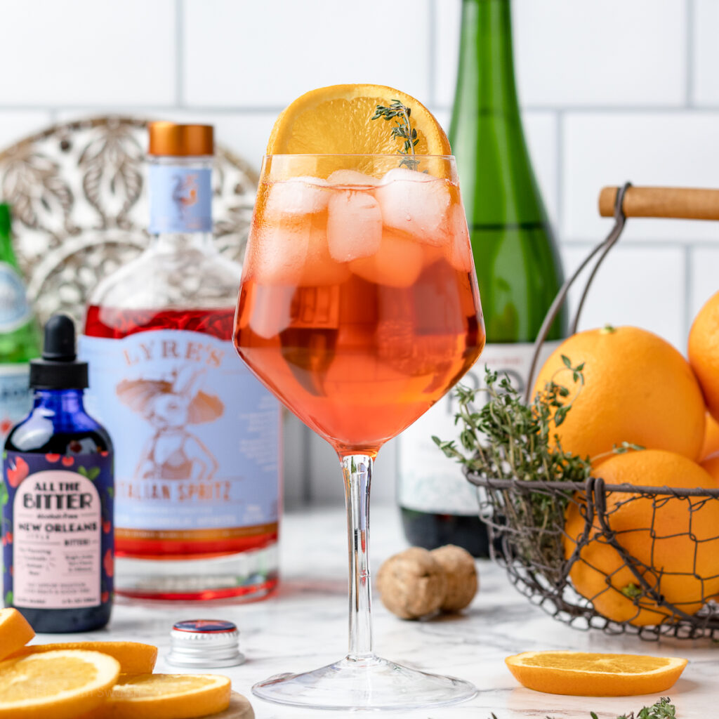 A cold glass of Aperol spritz garnished with lemon slices and thyme.