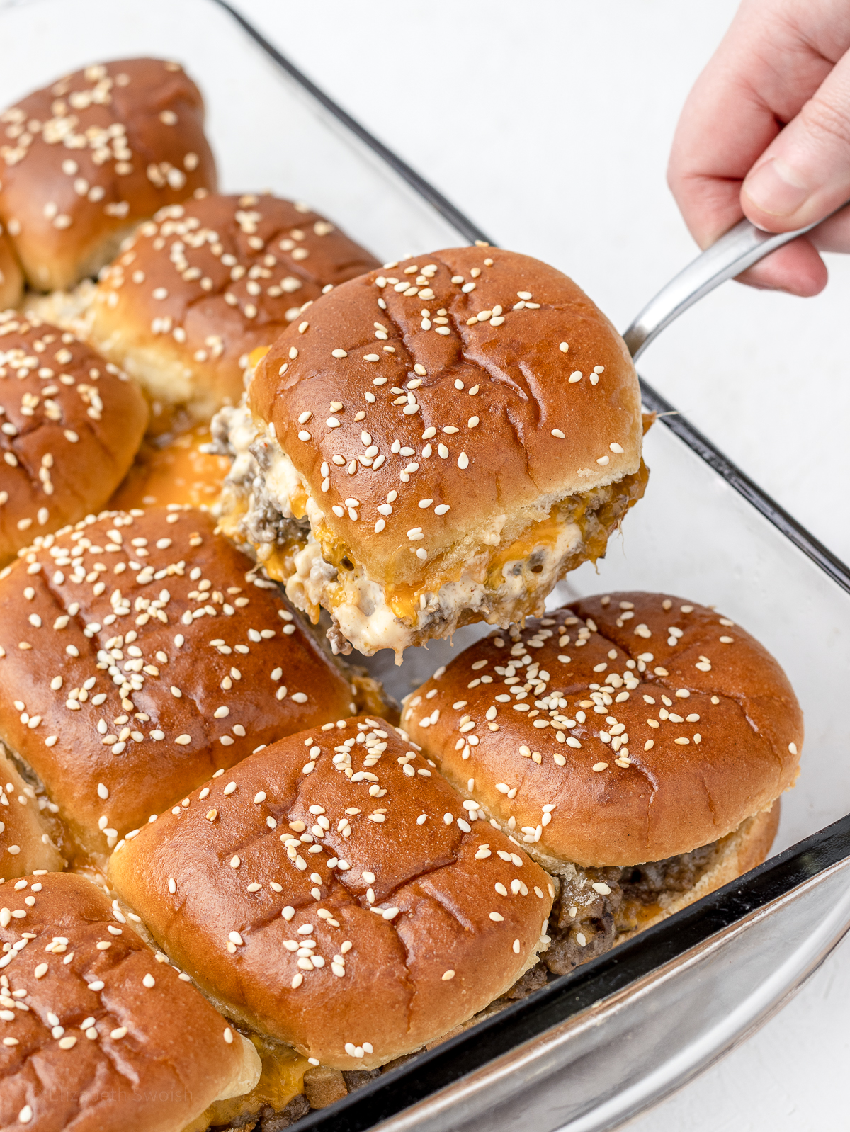 Toasty sliders in a baking pan with a hand lifting one from the pan.