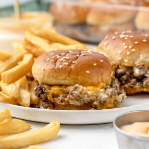A plate of gooey and delicious ground beef cheesy sliders with french fries and sriracha aioli.