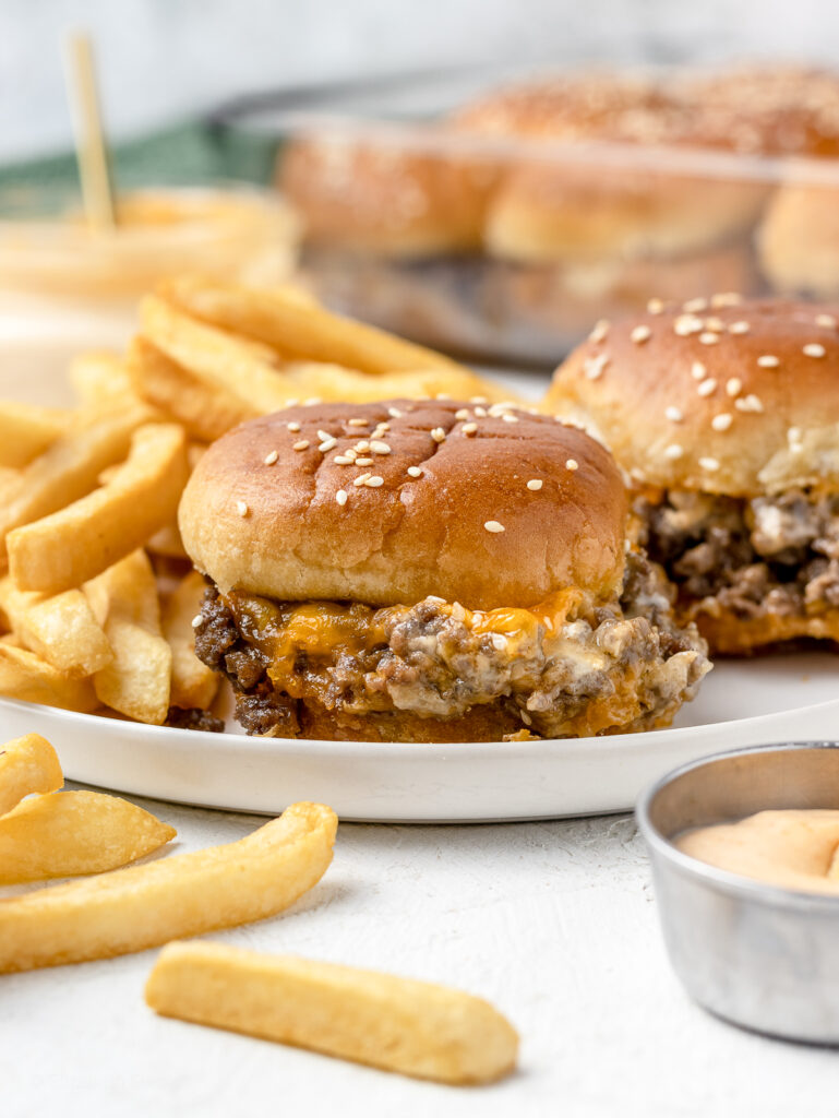 A plate of ground beef cheesy sliders with french fries and sriracha aioli.