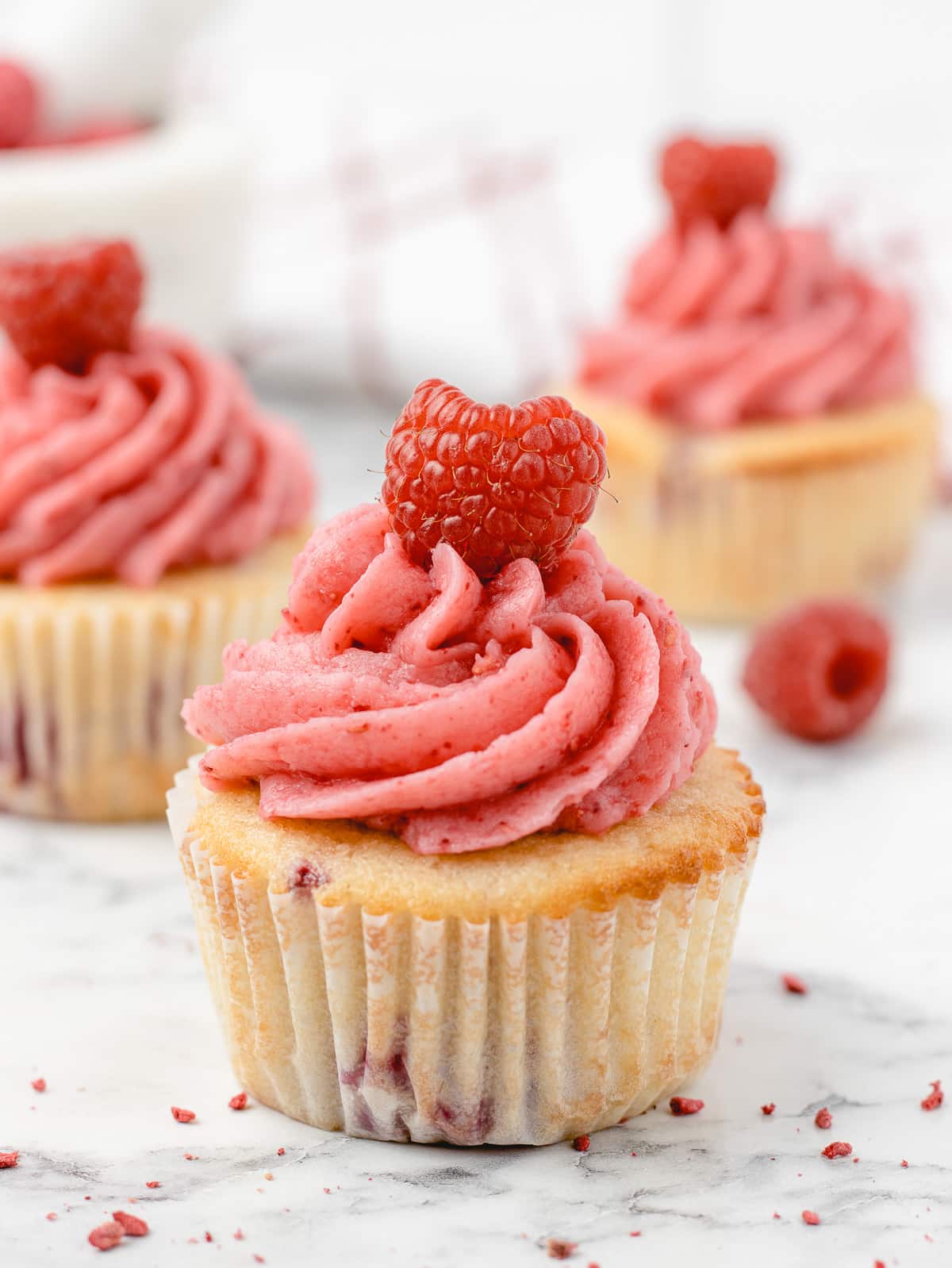 Cupcakes filled with fresh raspberries, topped with raspberry buttercream, and garnished with a fresh raspberry.