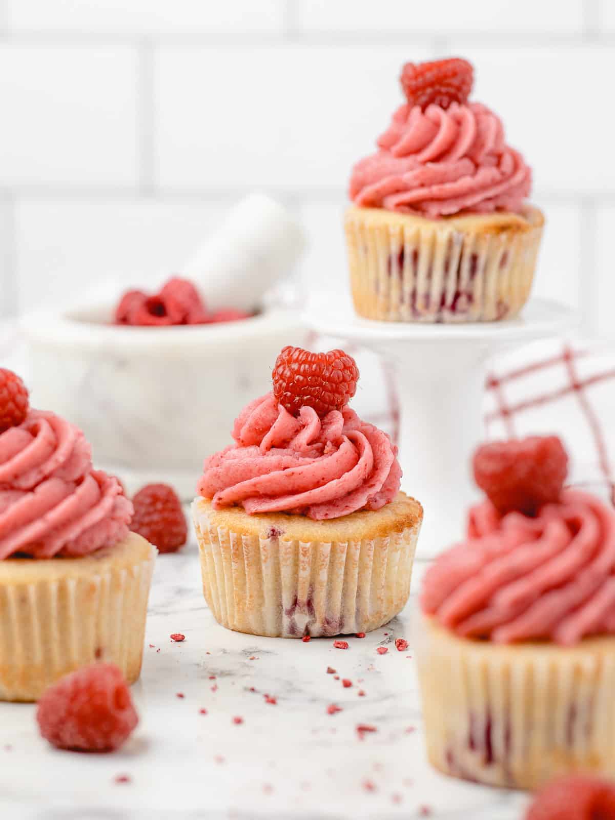 Decorated cupcakes surrounded by freeze dried raspberry powder and fresh raspberries.