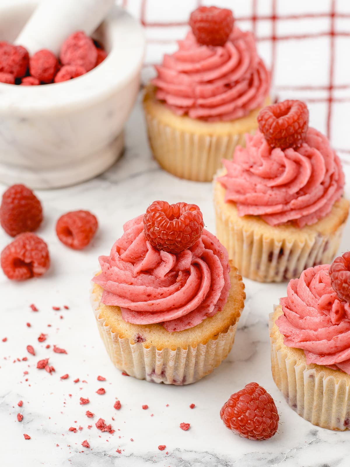 Raspberry Cupcakes decorated with fresh raspberries and freeze dried raspberries in a mortar and pestle.