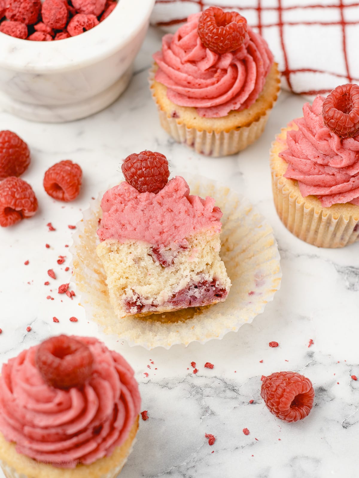 Unwrapped and sliced in half Raspberry Cupcake with more cupcakes surrounding it.