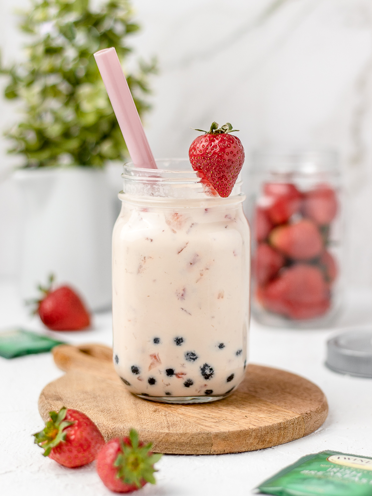 Layers of sweet strawberry, boba, tea, and milk in a jar. Garnished with a fresh strawberry and large pink boba straw.