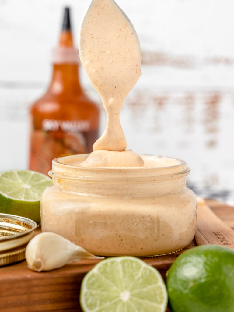 Spoon drizzling creamy sriracha sauce.