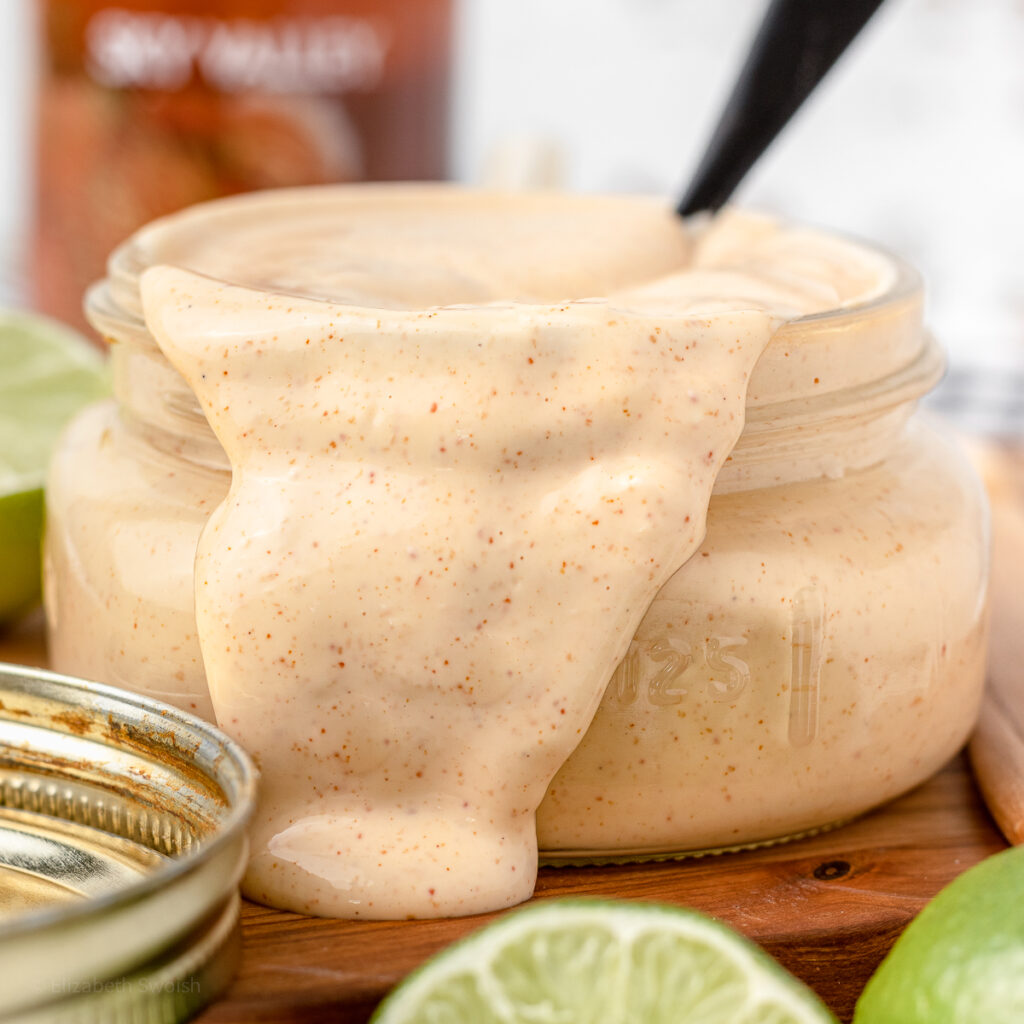 Spicy and creamy Sriracha Aioli sauce dripping out of the container with lime slices on the side.