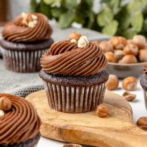 Nutella cupcakes with swirls of creamy hazelnut buttercream surrounded by hazelnuts and Nutella.