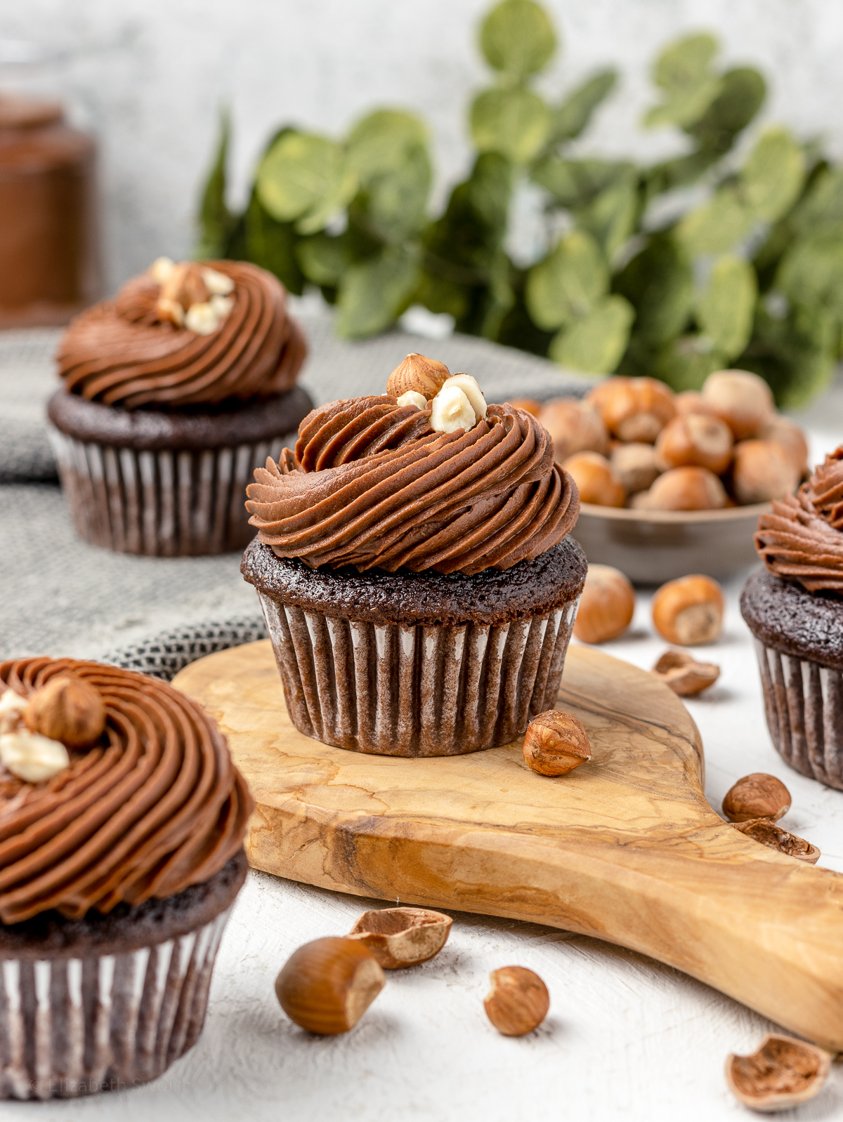 4 Nutella cupcakes surrounded by hazelnuts, nutella, and chocolate hazelnut buttercream.