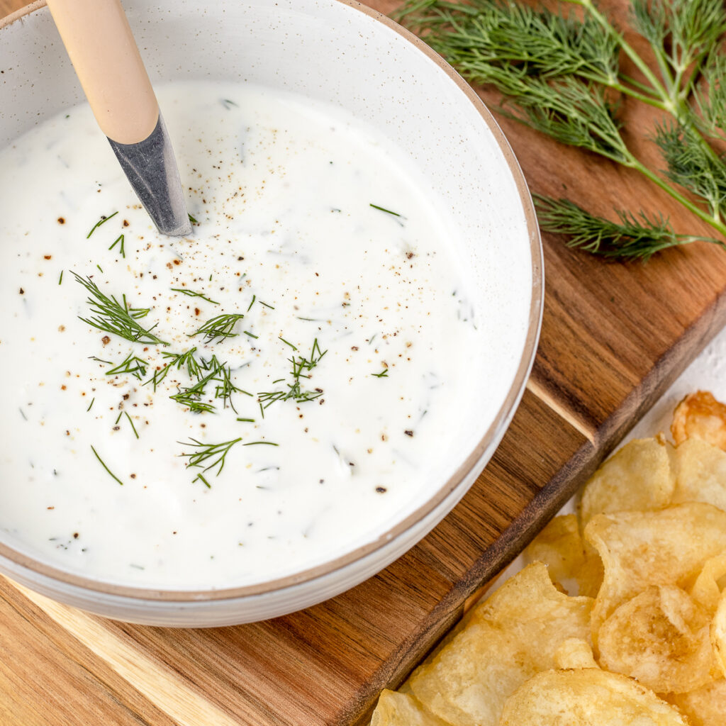 Bowl of Yogurt Dill Sauce with a spoon and potato chips on the side.
