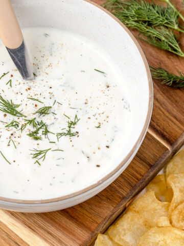 Bowl of Yogurt Dill Sauce with a spoon and potato chips on the side.