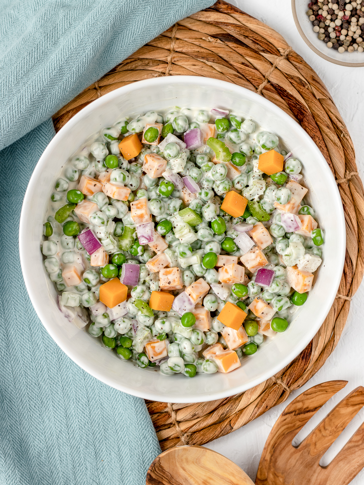 English Pea Salad in a large bowl topped with salt and pepper. Wood serving salad spoons on the side.