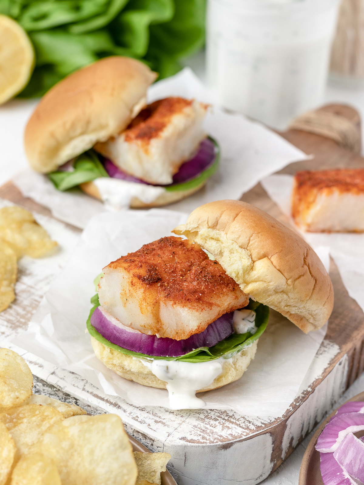 2 baked cod fish sliders with top buns on the side and flaky, paprika seasoned cod fish exposed.