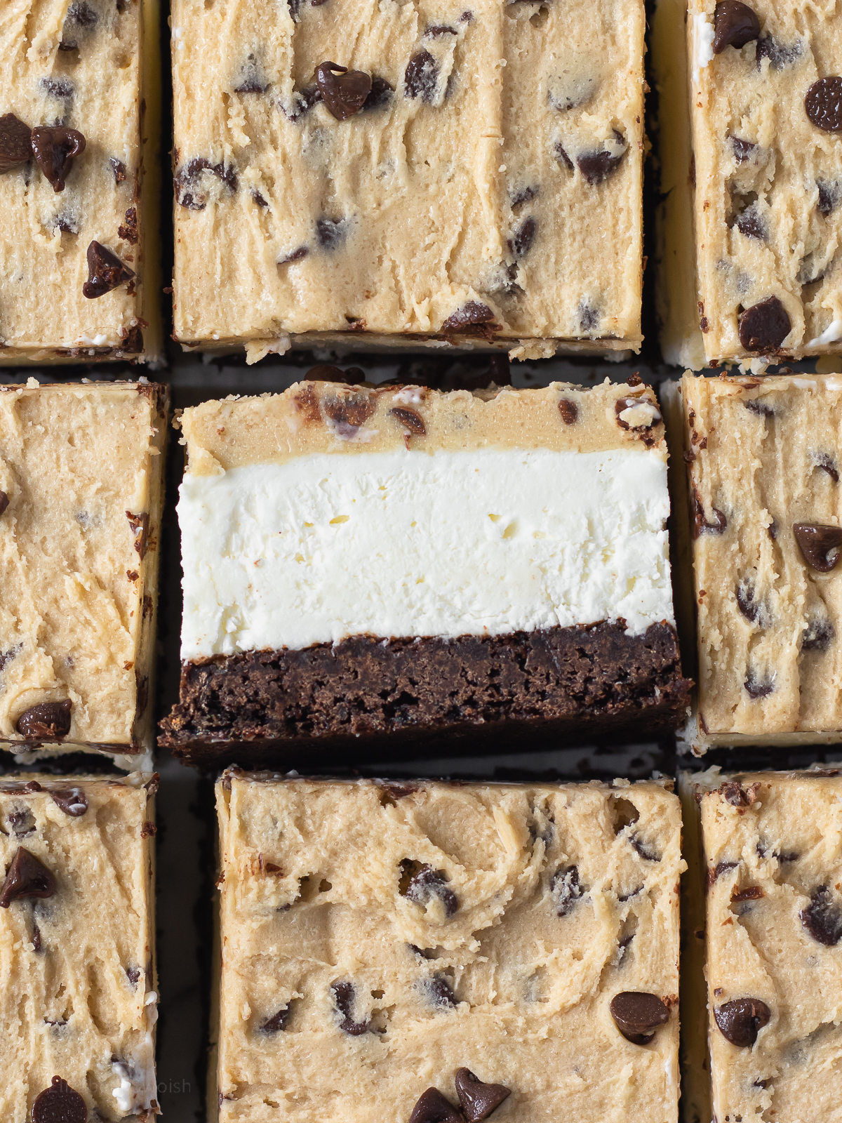Brownie Cookie Cheesecake Bar flipped on its side to see bottom brownie layer, middle no bake cheesecake, and top edible chocolate chip cookie dough.