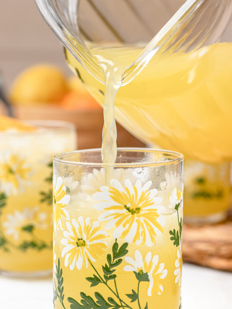 Pouring the lemonade over ice in a glass with daisy flowers painted on it.
