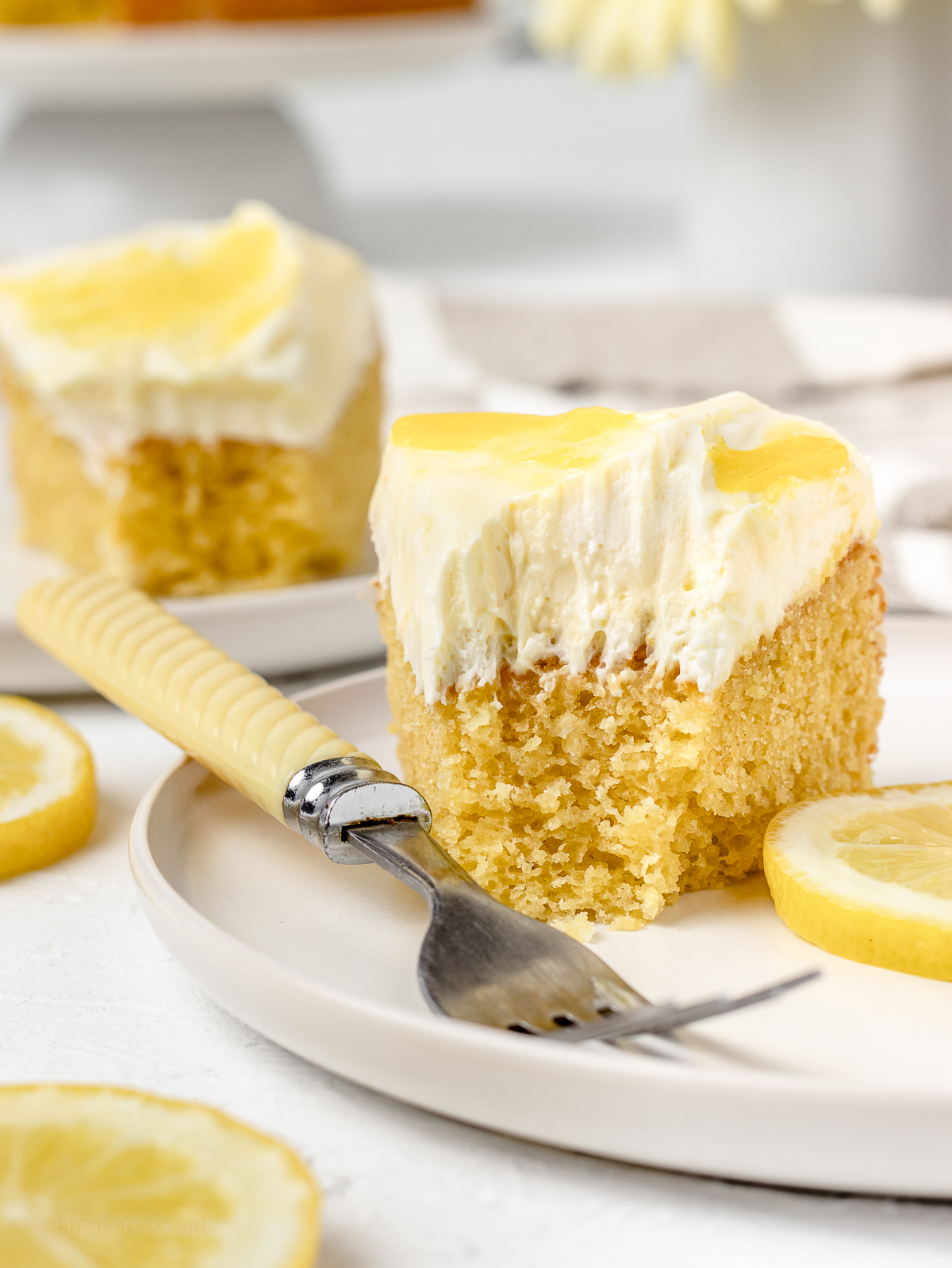 Two slices of cake with bites taken out of them and lemon slices on the side.