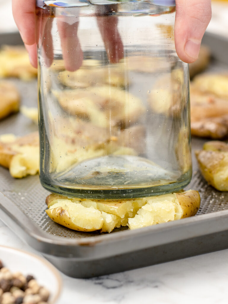 A large glass pressing down on and smashing a par boiled fingerling potato.