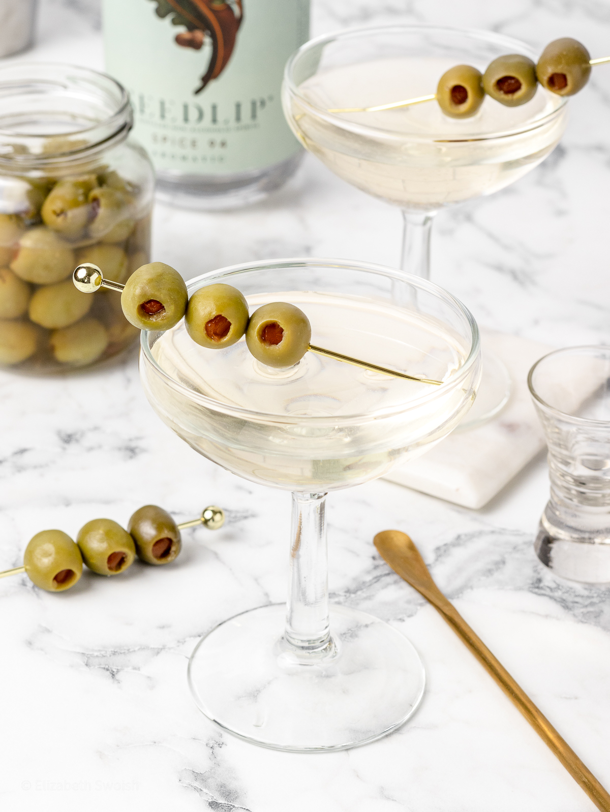 Non Alcoholic Dirty Martini Mocktail in a martini glass garnished with olives.