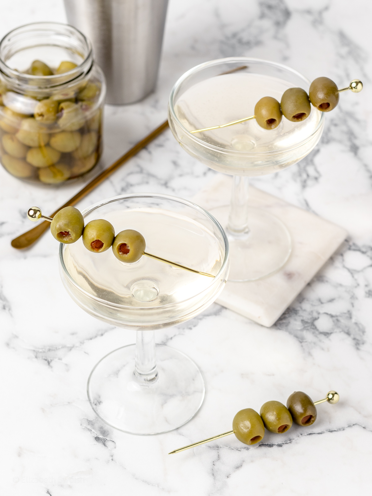 2 Non Alcoholic Dirty Martini Mocktails with an olive garnish ready to drink.