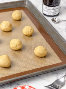 Large balls of lemon cookie dough on a lined baking sheet.