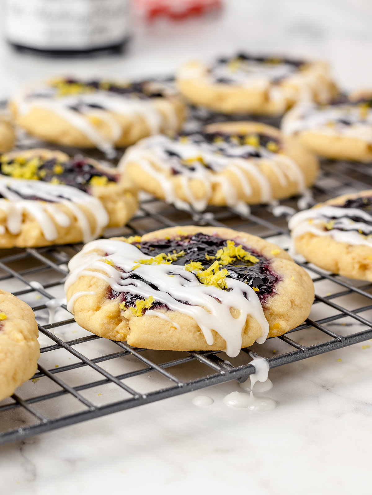 Lemon Blueberry Cookies topped with blueberry jam, lemon glaze, and lemon zest on a cooling rack.