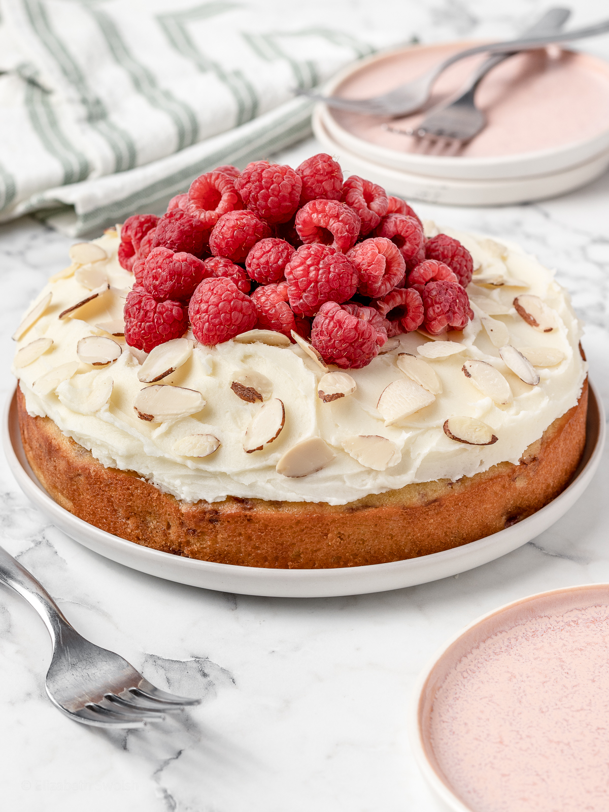Raspberry and Almond Cake topped with fresh raspberries and almond slices. Forks and plates on the side, ready for eating.
