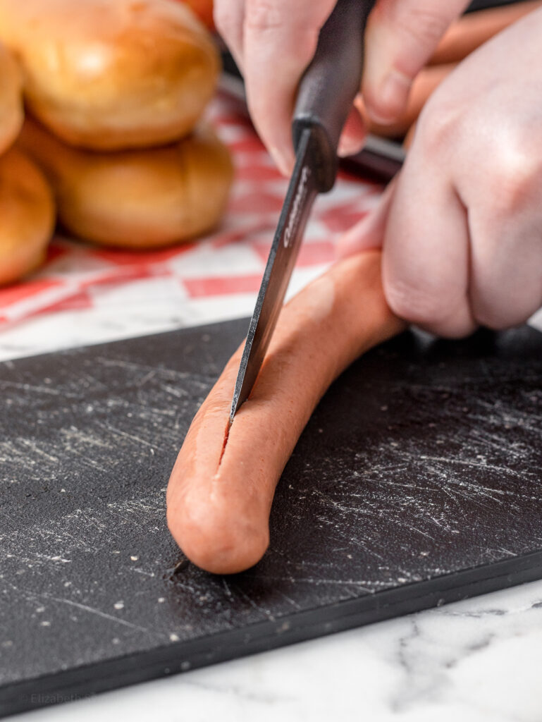 Scoring hot dogs with a sharp knife so the smoke can penetrate the meat.