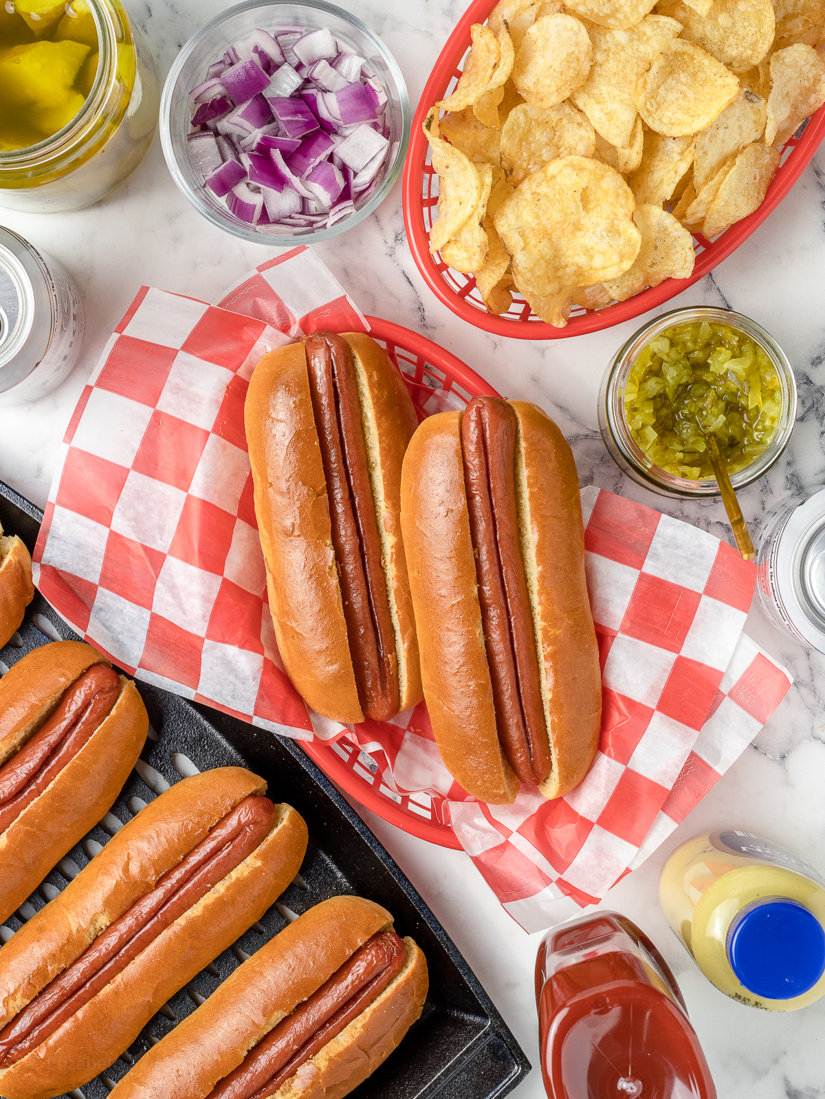 Smoked Hot Dogs in a basket ready to be topped with toppings and more hot dogs on the side.