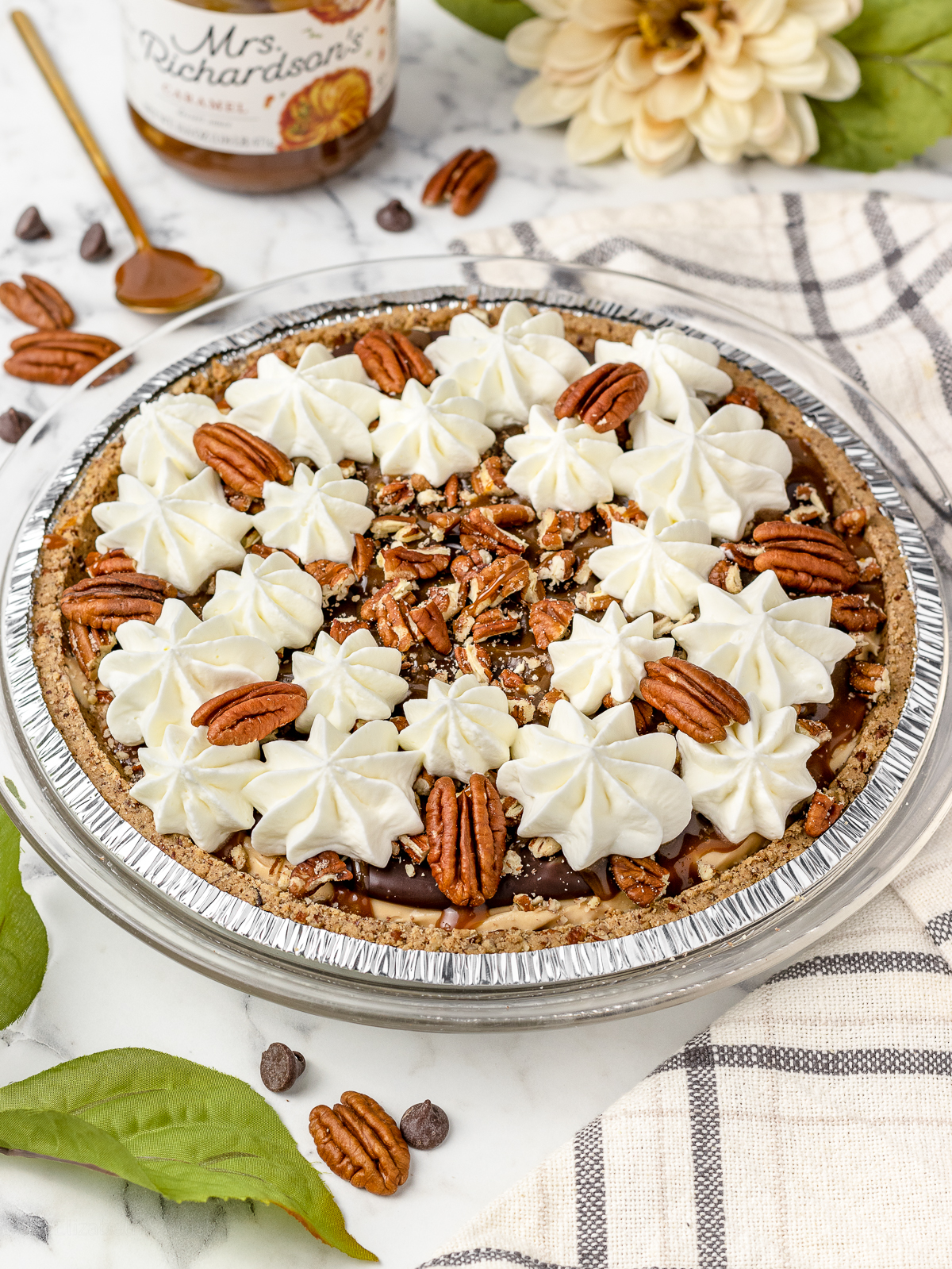 Pie topped with more caramel sauce, pecans, and whipped cream. Pecan halves and caramel cream sauce on the side.