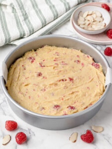 Almond cake batter with folded in fresh raspberries. Batter in prepared cake pan ready to bake.