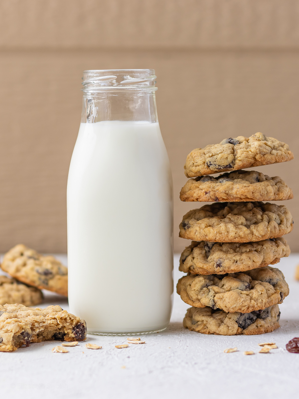Tall stack of old fashioned oatmeal raisin cookies with a glass of milk and a half eaten cookie on the side.