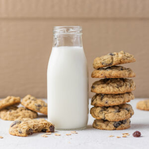 Tall stack of oatmeal raisin cookies with a glass of milk and a half eaten cookie on the side.
