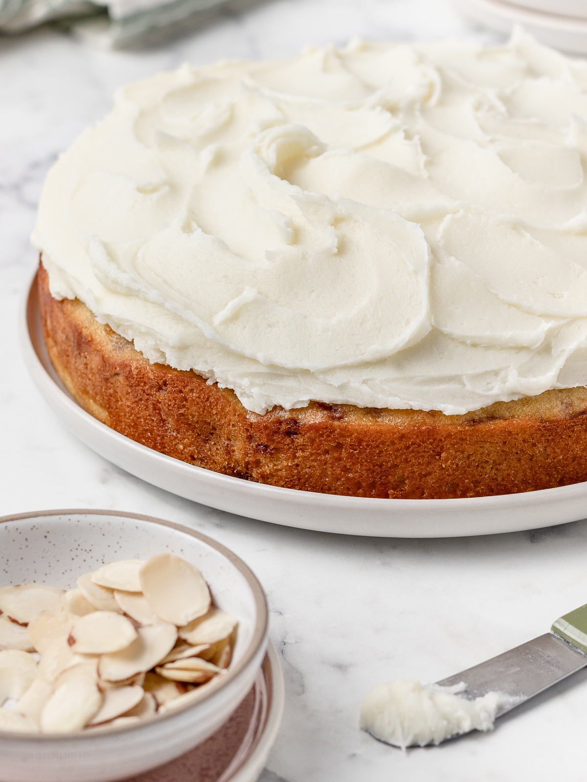 Fluffy Almond Frosting on top of a cake with slivered almonds on the side.
