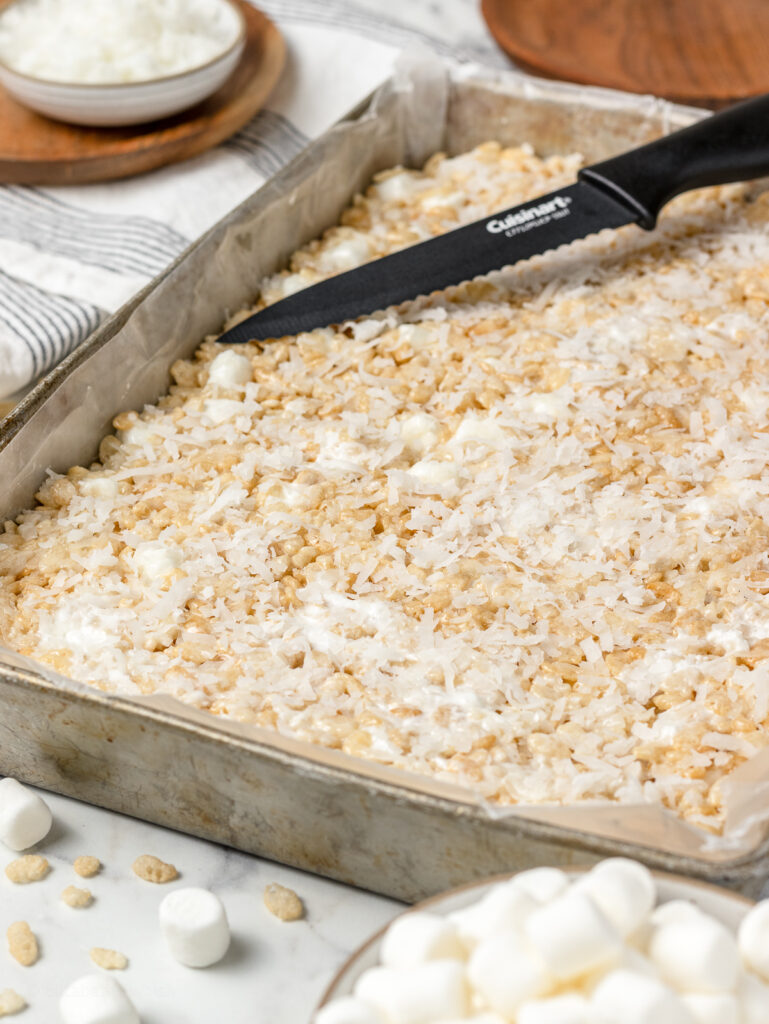 Coconut Rice Krispie Treats in a pan with the knife on the side ready to cut into squares.