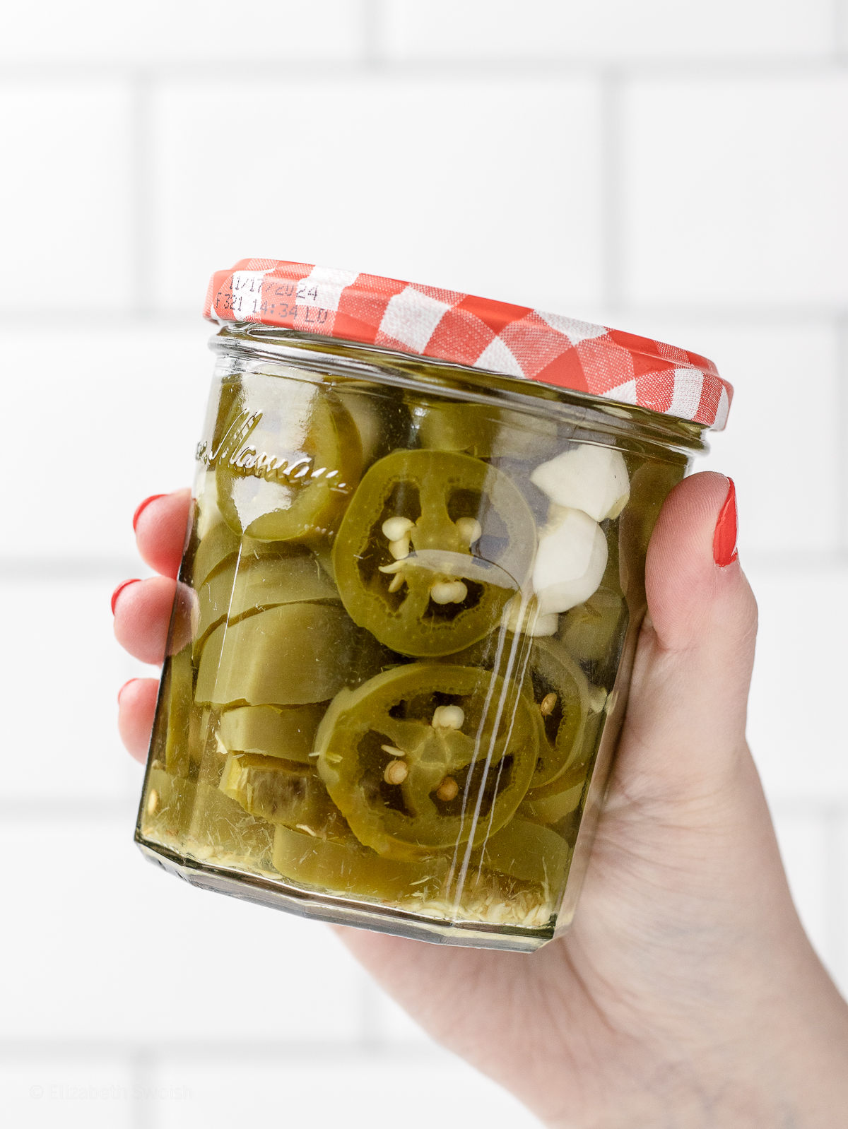 Hand holding onto a full jar of homemade Quick Pickled Jalapenos.
