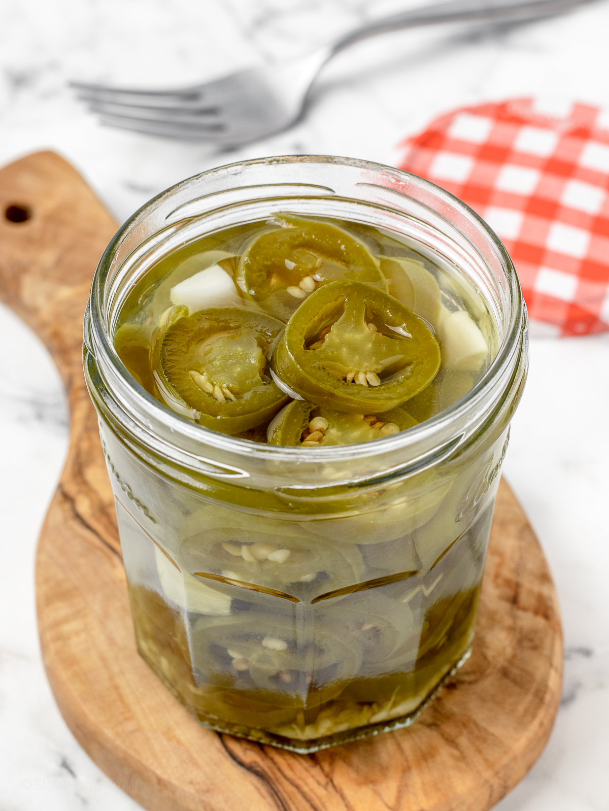 Jalapenos in a jar of brine with the lid and a fork on the side.