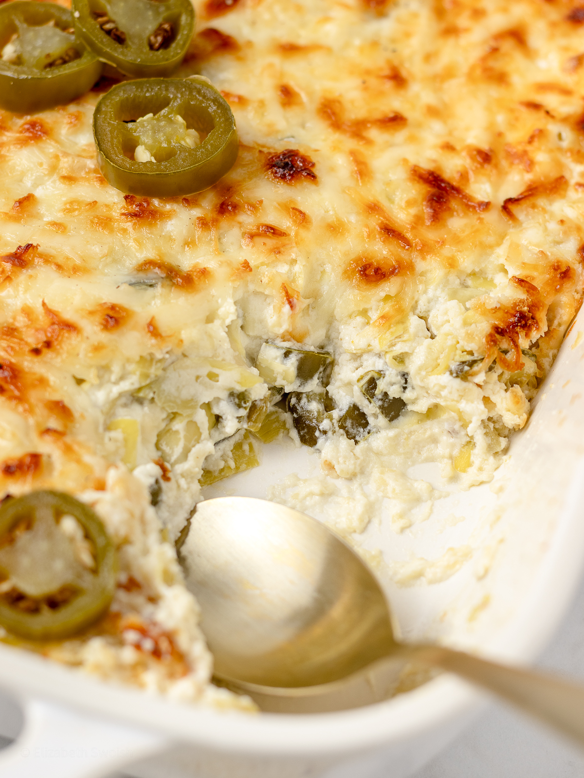 Jalapeno Artichoke Dip with spoon. Close up view to see the creamy dip with chunks of pickled jalapeno and artichoke hearts.