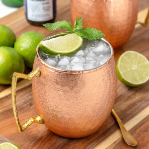 Non alcoholic Moscow Mule in copper mugs chilled with ice. Mocktail garnished with lime wedges and mint leaves.